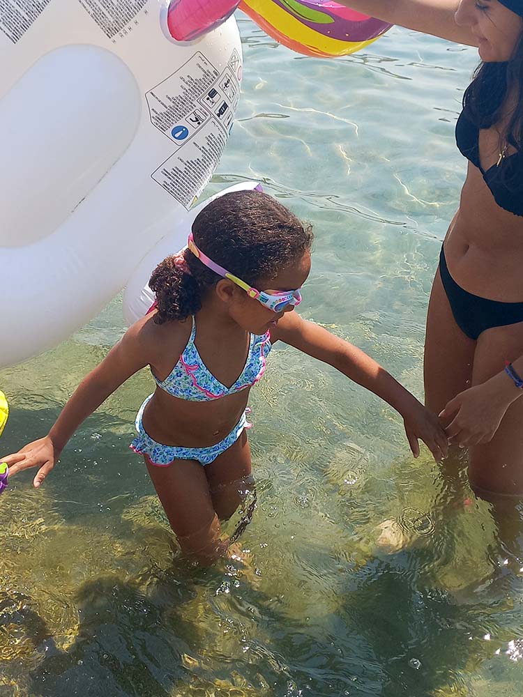 Young child holding a babysitter’s hand while playing in the sea in Sifnos