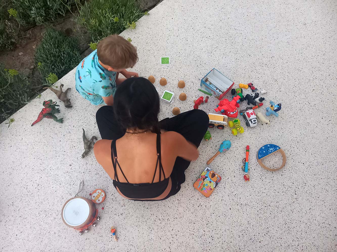 Babysitter playing with a toddler surrounded by toys during outdoor childcare activities in Sifnos