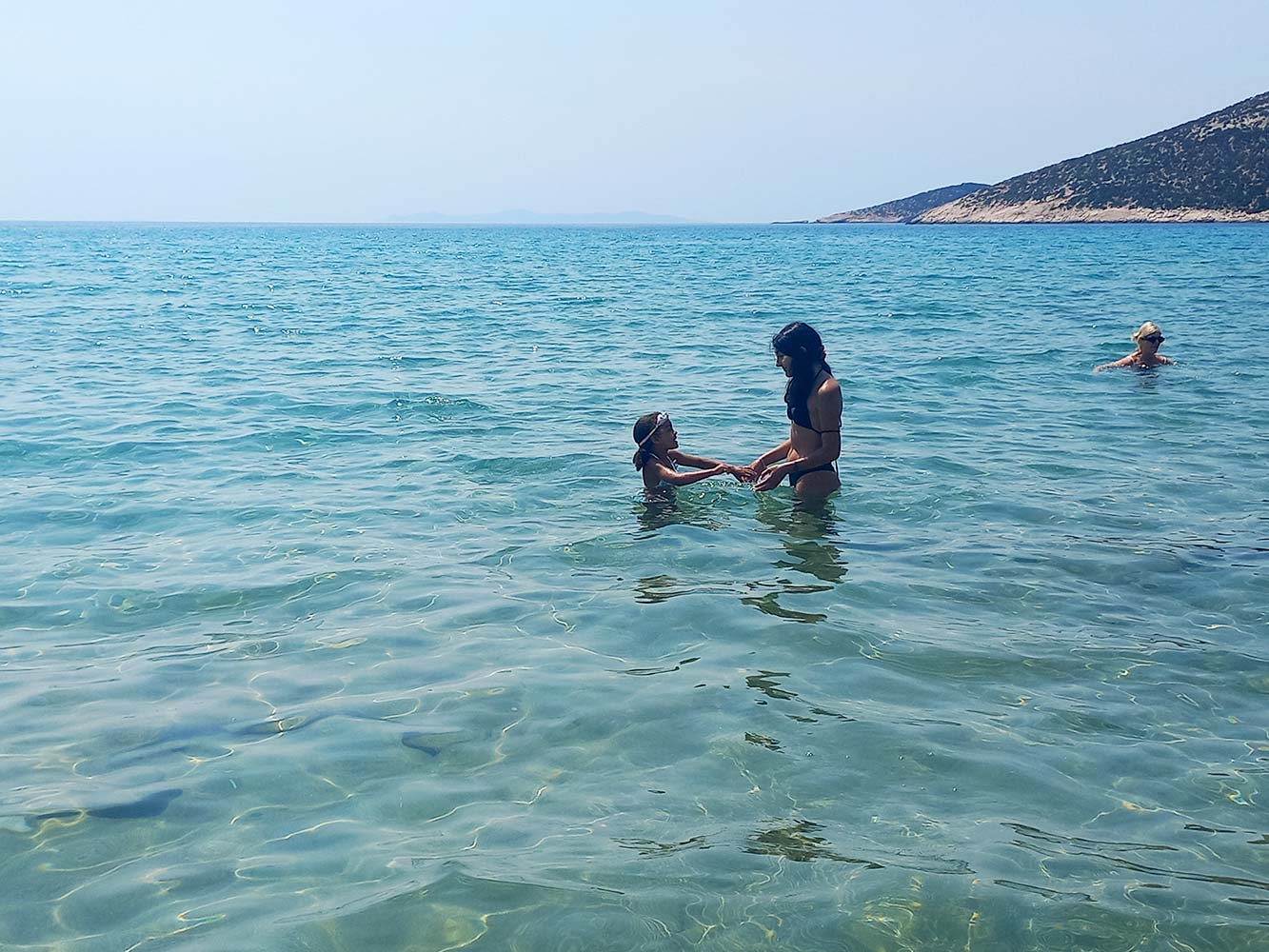 Child playing safely in the shallow sea with a babysitter on a beach in Sifnos